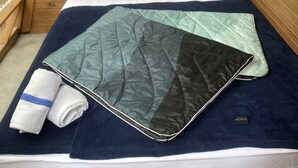 A bed with a quilt, pillows, and a towel in a wooden room with a window and a shelf with items. - Loblolly Pines 3 Adventure Aframe (Eureka Springs)