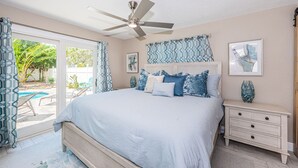 A bedroom with a bed, a nightstand, a ceiling fan, and a view of the outdoors. - Renovated new Pool Home (Indian Rocks Beach)