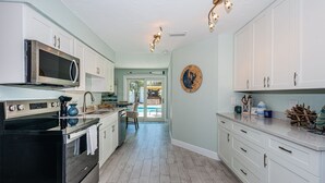 A modern kitchen with white cabinets, stainless steel appliances, and a wooden floor. - Renovated new Pool Home (Indian Rocks Beach)