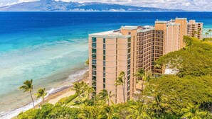 Un hotel frente a la playa con varios edificios altos, vista despejada del océano y montañas al fondo.