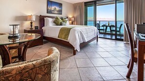 Habitación de hotel con cama, una mesita de vidrio, una silla, ventilador de techo y vista al océano.