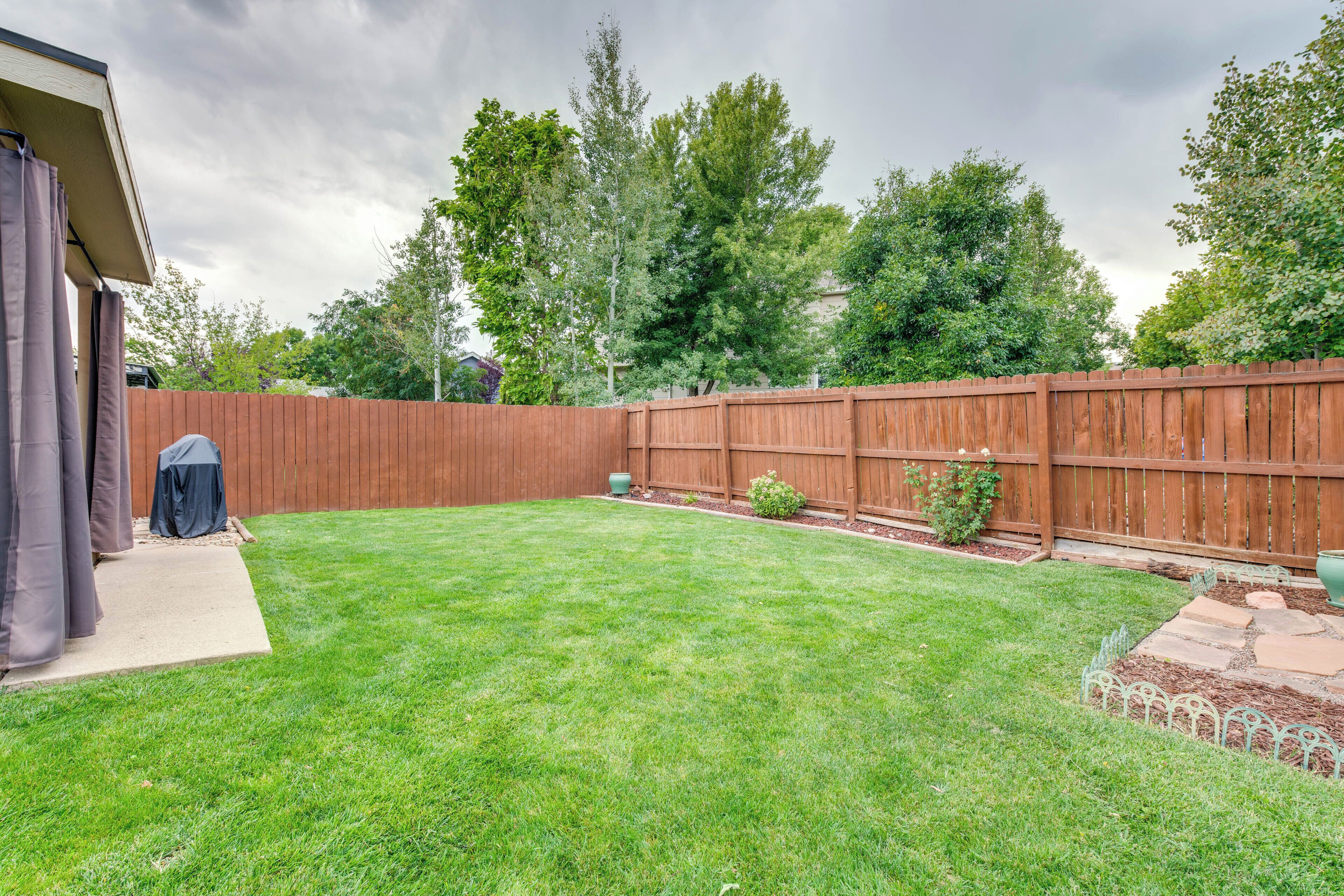 Un jardin avec une clôture en bois, une pelouse et un espace patio équipé d’un barbecue.
