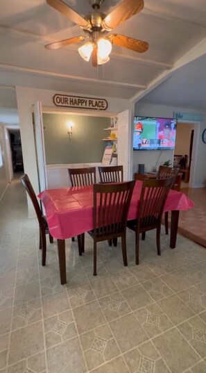 A dining area with a table covered in a red tablecloth, surrounded by wooden chairs. A ceiling fan is visible above, and a sign above the table reads "OUR HAPPY PLACE". - Charming 2-bedroom house by the lake in Dover TN (Dover)