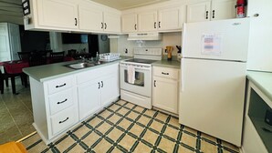 Una cocina compacta con gabinetes blancos, estufa, lavabo y refrigerador.