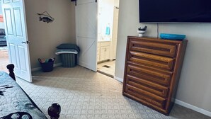 Un dormitorio con cama, cómoda, televisor y puerta corredera que da a un baño.