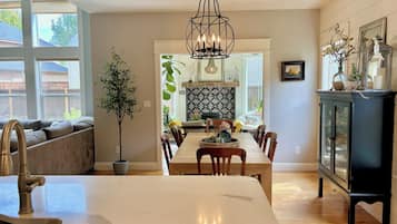 Una cocina moderna con una isla de mármol, una mesa de comedor de madera y sillas. Se observa un armario negro con puertas de vidrio y una lámpara colgante.