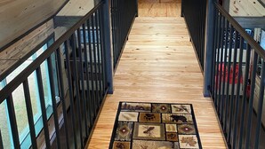 Un intérieur en bois avec un escalier central, un lit recouvert d’une courtepointe à carreaux rouges et noirs, et un tapis à motifs.
