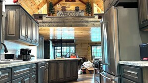 Une cuisine spacieuse avec un plafond en bois, un îlot central et une pancarte « BIENVENUE » au-dessus de la porte.
