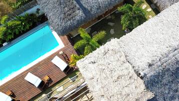 Área de piscina com guarda-sóis de palha, deck de madeira e espreguiçadeiras.