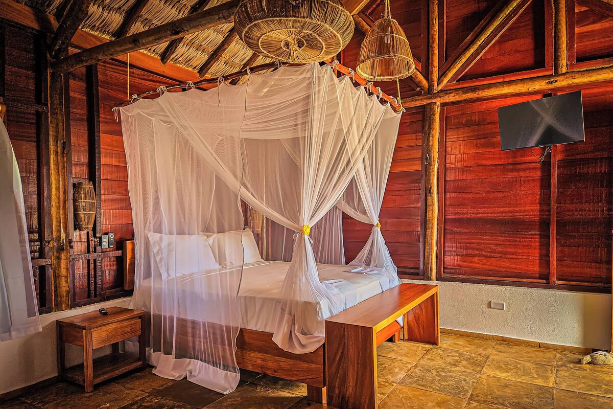 Ein hölzernes Himmelbett mit Baldachin, ein Nachttisch aus Holz und ein Boden mit Steinfliesen.