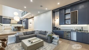 A modern kitchen with dark cabinets, a built-in wine rack, and a dining area with a high table and chairs.