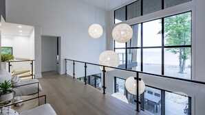 A spacious interior with a high ceiling, large windows, and modern pendant lighting.