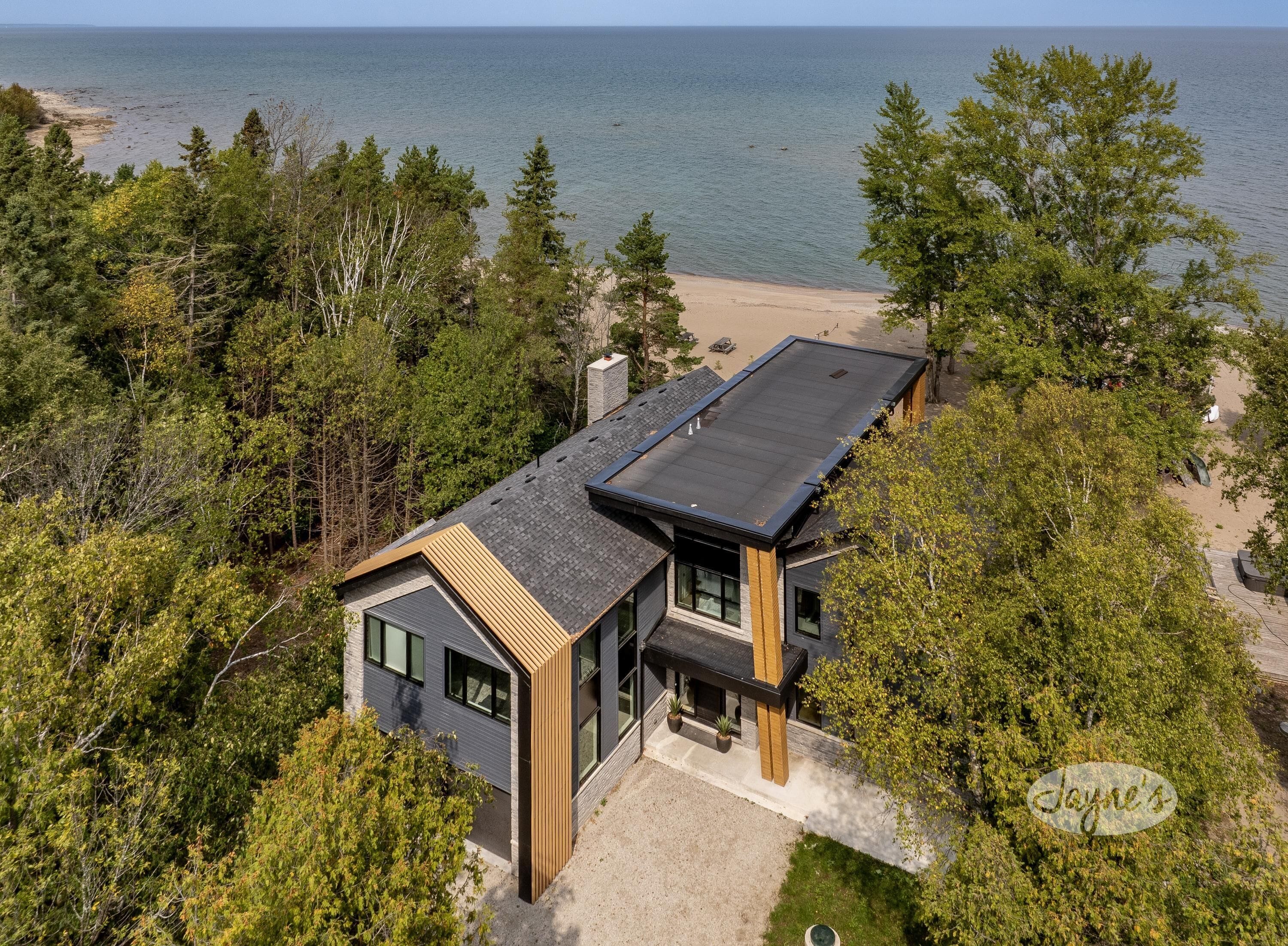 Una casa moderna con una amplia terraza, rodeada de un bosque denso y una playa.