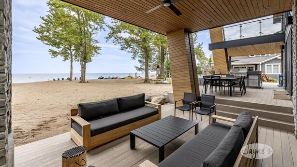 A covered outdoor seating area with a wooden deck, a black sofa, a coffee table, and a grill.