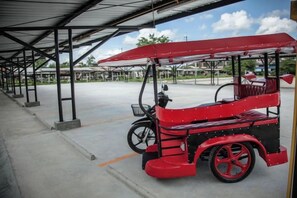 Un coche clásico rojo aparcado bajo un porche, con cielo despejado al fondo.