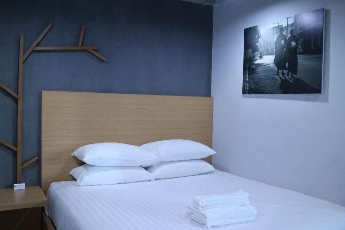 A neatly made bed with white linens and pillows, a wooden headboard, and a framed artwork on the wall.