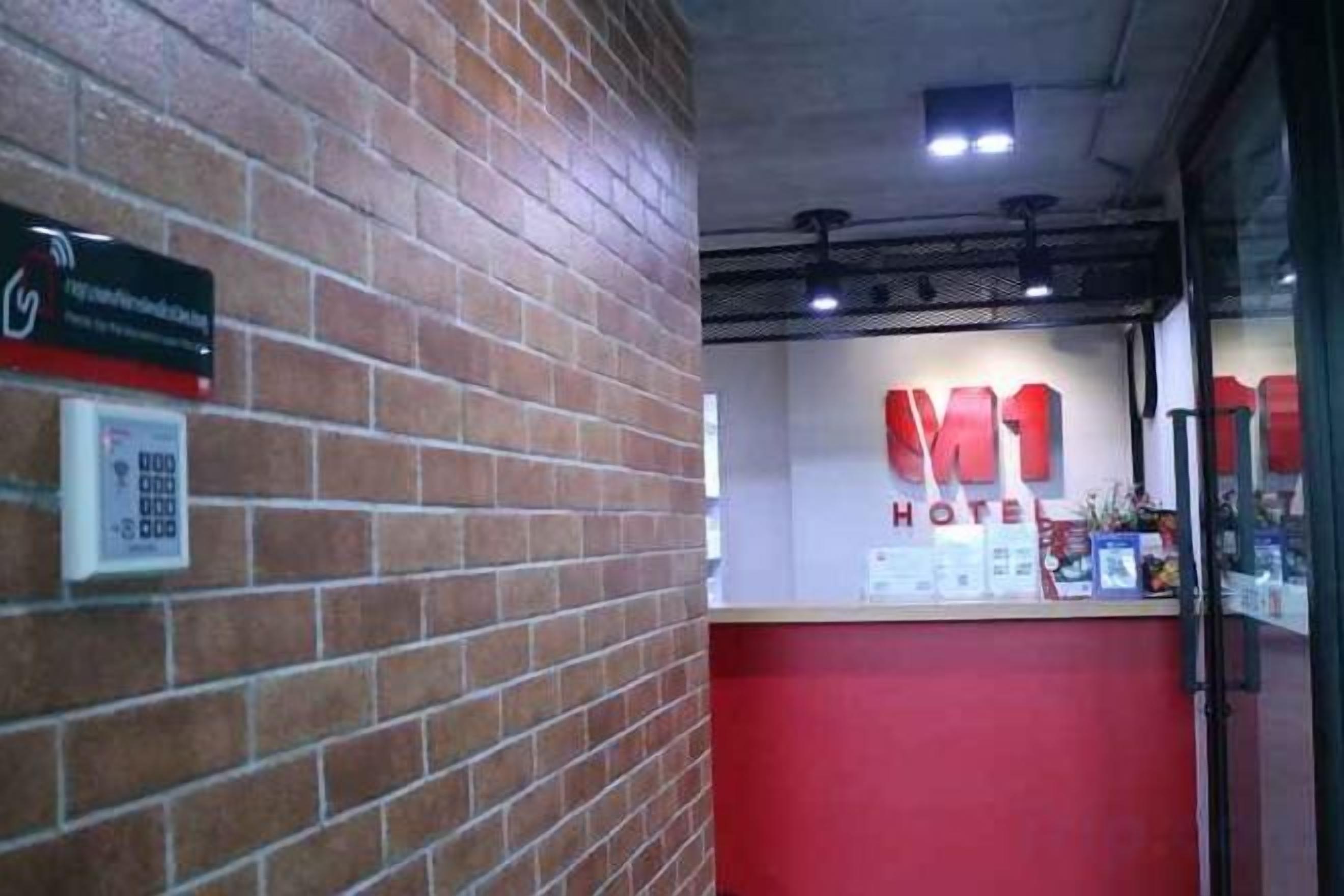 A hotel reception area with a brick wall, a red counter, and a sign that reads 'HOTEL'.