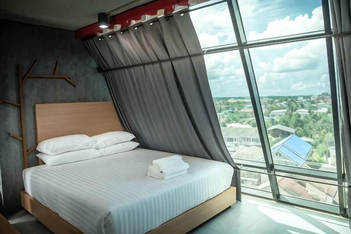 A modern bedroom with a large bed, a view of the city, and a window with curtains.