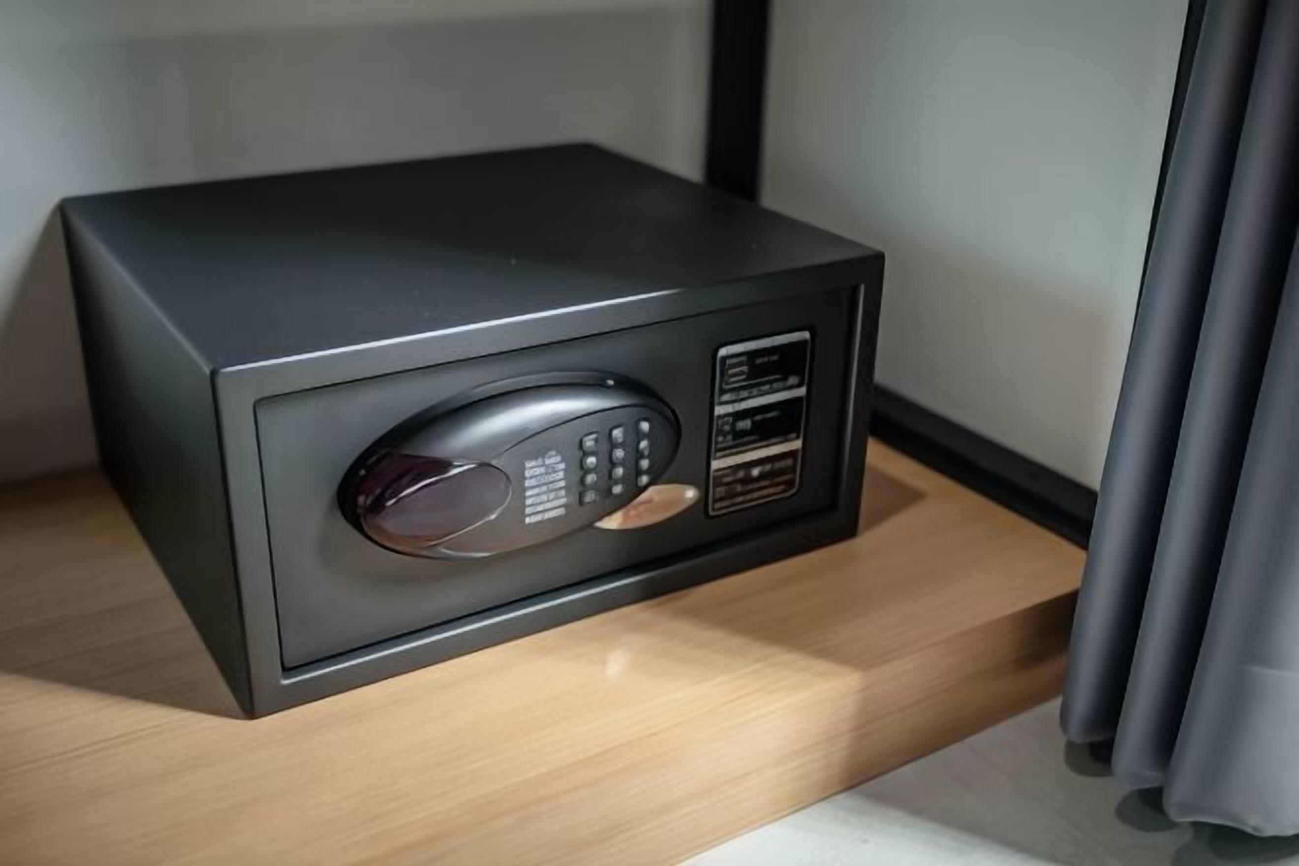 A black safe with a keypad and a glass window, placed on a wooden shelf.