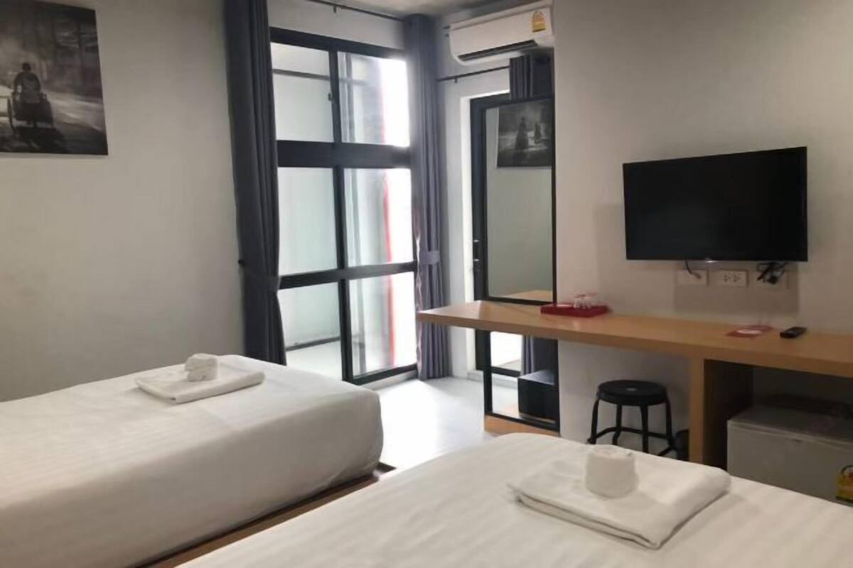 Habitación de hotel con dos camas, un escritorio con televisor, un espejo y una ventana con cortinas.