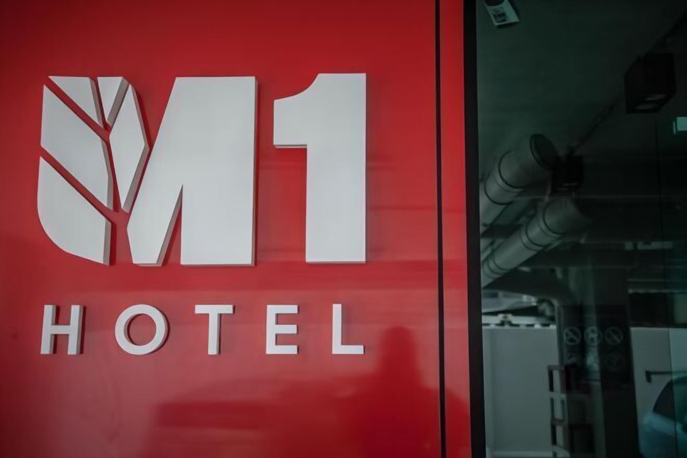 A red wall with the M1 Hotel logo and the word "HOTEL" below it.