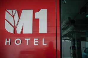 A red wall with the M1 Hotel logo and the word "HOTEL" below it. - M1 Hotel (Nakhon Si Thammarat City)