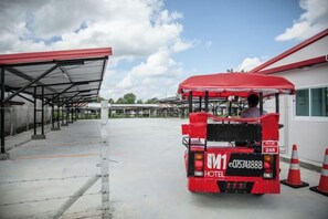 Een rode bus met een nummerplaat en een hotelsignaal, geparkeerd bij een bushalte met een overdekte beschutting en een gebouw op de achtergrond.