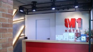 Un taulell de recepció amb un panell vermell, una porta blanca i un senyal que diu "M1 HOTEL".