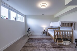 Un dormitorio con una cama nido, un telescopio, una lámpara y un ventanal grande.