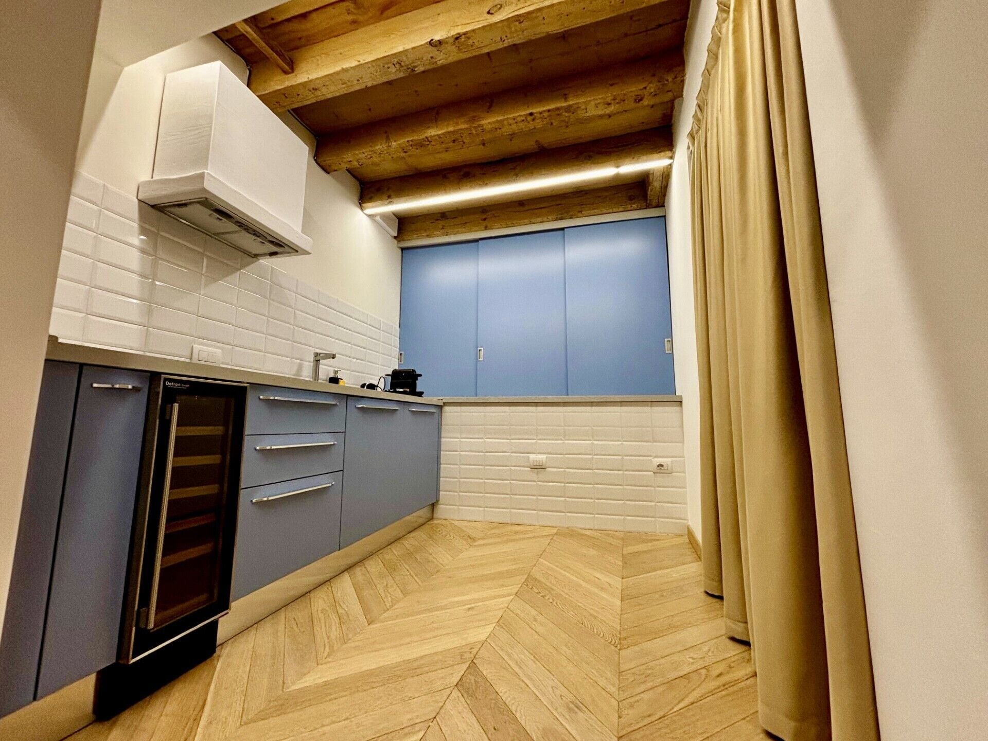 A kitchen with a herringbone floor, a built-in oven, and a blue cabinet.