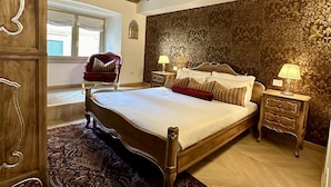 A bedroom with a wooden ceiling, a large bed with multiple pillows, a nightstand with a lamp, and a patterned rug.
