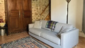 Ein Wohnzimmer mit grauem Sofa, einem gemusterten Teppich, einem Holzschrank und einer Steinwand.