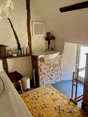 A rustic bathroom with a stone sink, wooden beams, and a patterned rug.