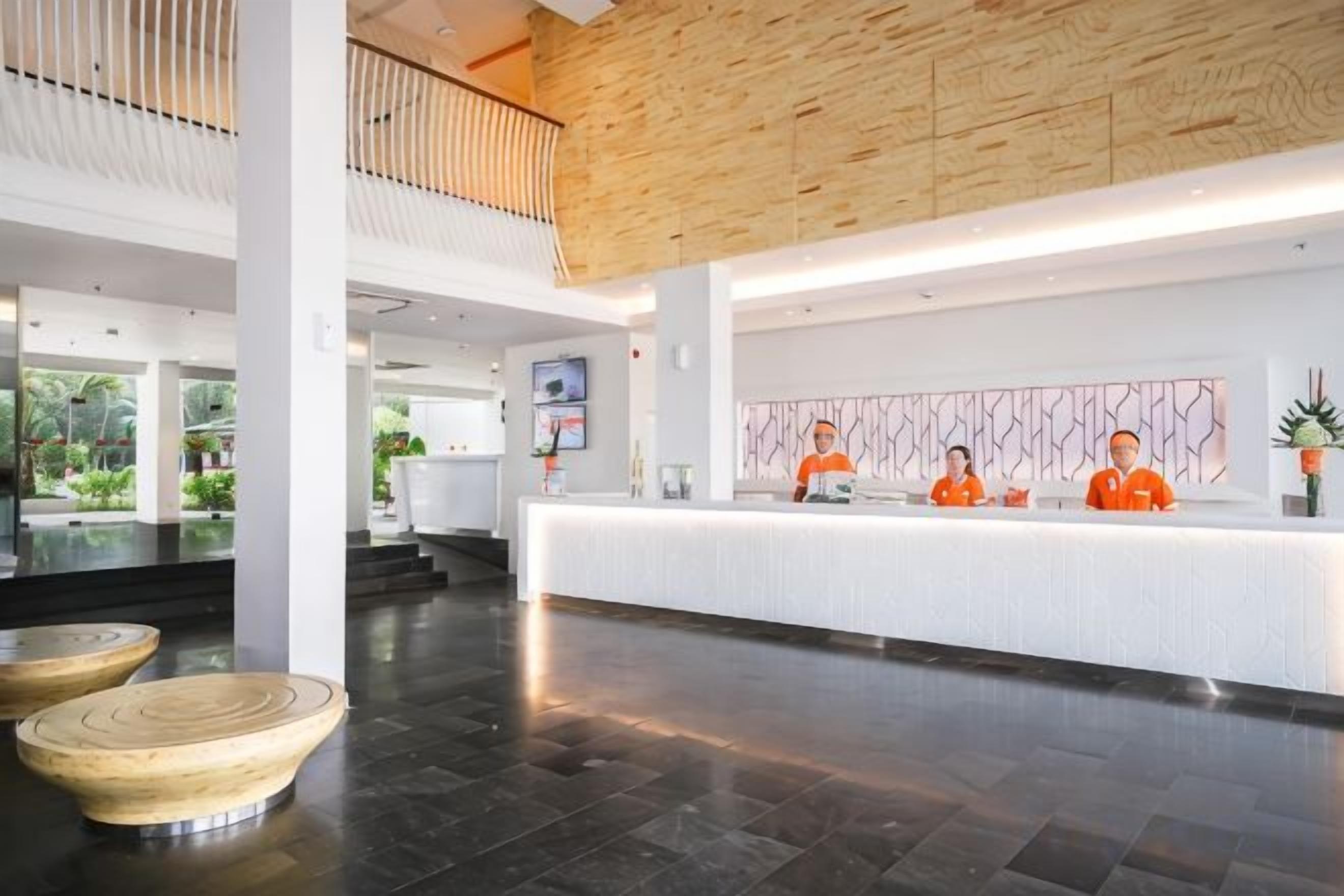 A hotel reception area with a modern design, featuring a reception desk, a wooden ceiling, and a view of the outdoors.