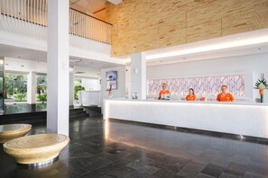 A hotel reception area with a modern design, featuring a reception desk, a wooden ceiling, and a view of the outdoors.