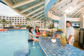 An indoor swimming pool with a bar area, lounge chairs, and a poolside restaurant. - Harris Resort Waterfront Batam (Sekupang)