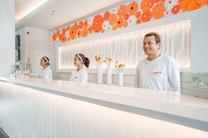 Ein Empfangsbereich mit einer weißen Theke, Mitarbeitern in weißen Uniformen und orangefarbenen Dekorationselementen an der Wand.