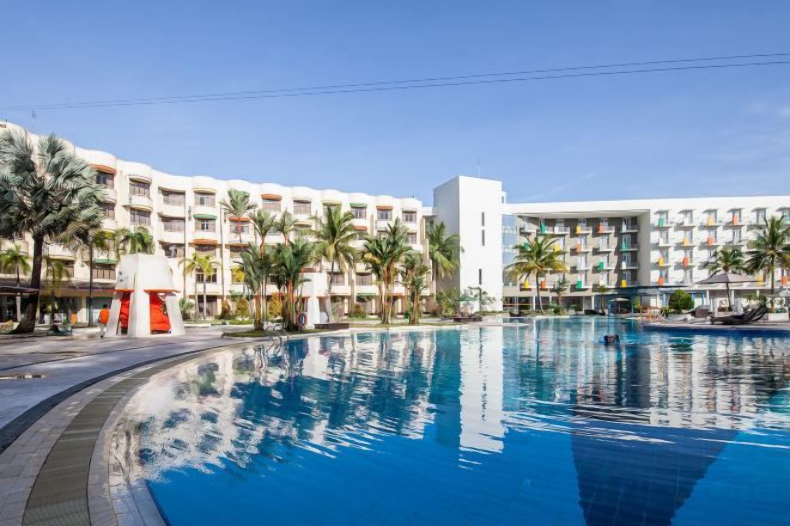 Un hôtel doté d’une piscine, de palmiers et surplombant un ciel bleu azur.