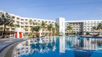 A hotel with a swimming pool, palm trees, and a clear blue sky.