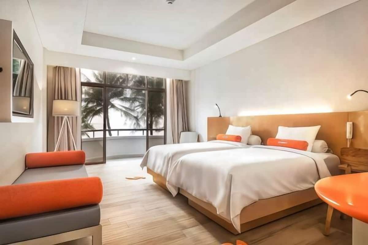 A modern hotel room with a large bed, a desk, and a view of palm trees through the window.