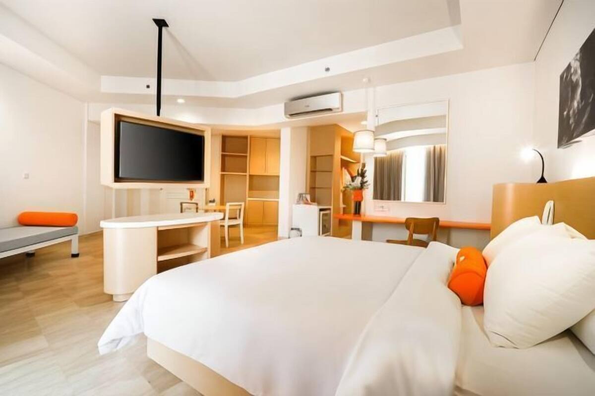 A modern hotel room with a large bed, a desk, a television, and a wardrobe.