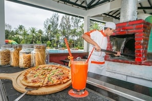 Eine Pizza auf einem Holzbrett, ein Getränk mit Trinkhalm und ein Backofen aus Ziegelsteinen.