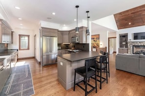 Enjoy cooking in the central island kitchen with stainless steel appliances and pendant lighting, complemented by a cozy seating area with a fireplace and large TV.