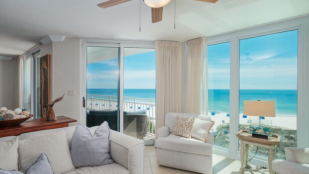 A spacious living room with a large sliding glass door leading to a balcony with a view of the ocean. There are two sofas and a small table with a lamp. - BEACHFRONT! OPEN CONCEPT! STUNNING 3 walls of  GLASS! (Pensacola)