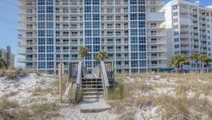 A multi-story hotel with a modern design, featuring balconies on each floor and a sandy beach area in front. - BEACHFRONT! OPEN CONCEPT! STUNNING 3 walls of  GLASS! (Pensacola)