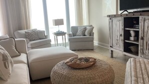 A living room with a sofa, armchair, ottoman, and a rustic wooden cabinet. - BEACHFRONT! OPEN CONCEPT! STUNNING 3 walls of  GLASS! (Pensacola)