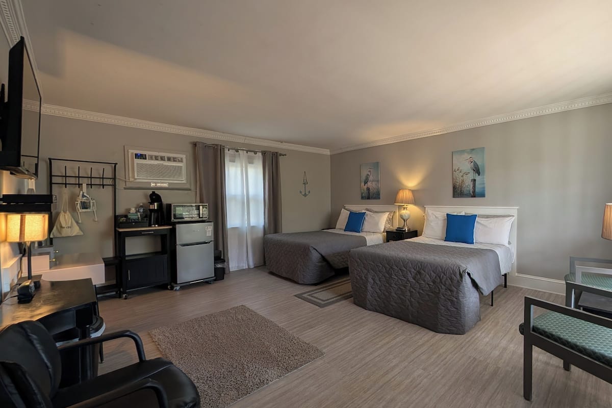 A hotel room with two beds, a desk with a computer, a refrigerator, a TV, and a window with curtains.