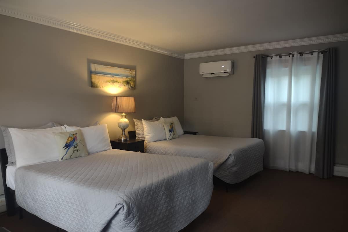 A hotel room with two beds, a painting on the wall, an air conditioning unit, and a window with curtains.