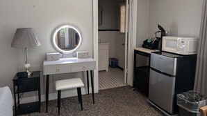 Ein kleines Hotelzimmer mit Schminktisch, Spiegel, Lampe, Kühlschrank und Mikrowelle.
