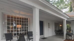 Eine überdachte Veranda mit Tisch und Stühlen, ein Fenster mit Lampe und eine Tür.